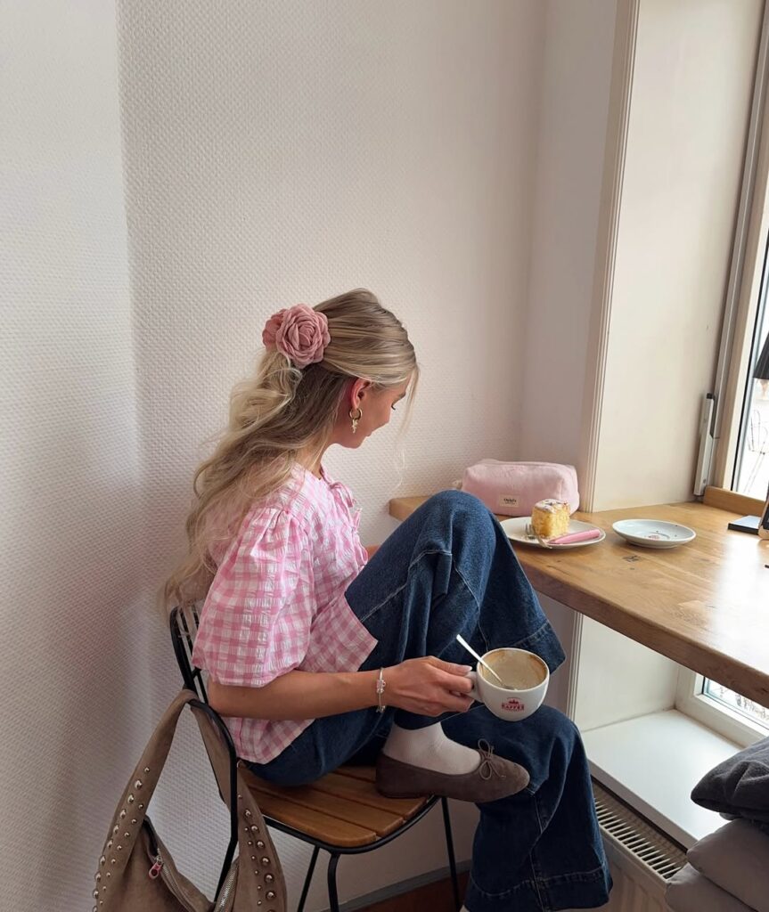 Vintage café style with a pink gingham puff-sleeve blouse, wide-leg jeans, taupe ballet flats with white socks, and a large rose hair clip.