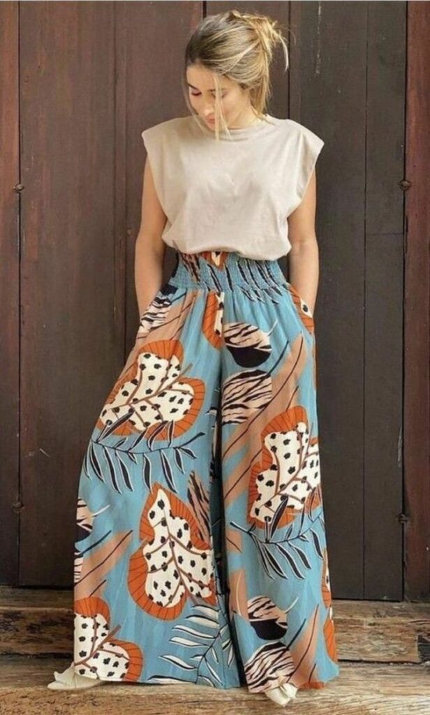Tropical wide-leg pants look with a neutral padded-shoulder tank tucked into high-waisted printed pants in earthy tones and palm leaf motifs.