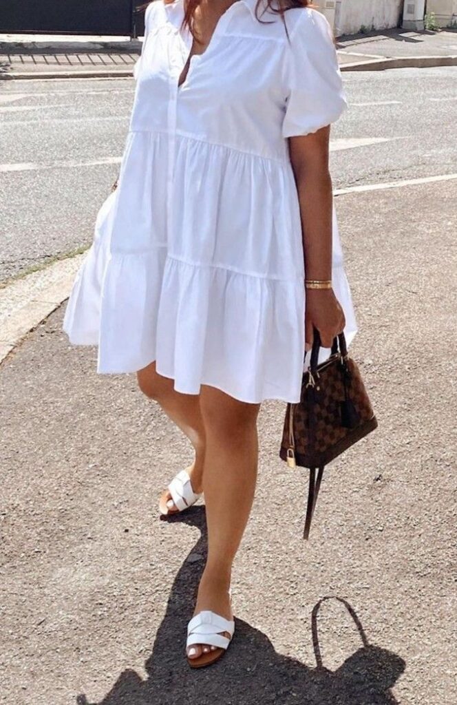 Airy white babydoll dress paired with white criss-cross flat sandals and a small Louis Vuitton top-handle bag, worn on a sunny sidewalk.