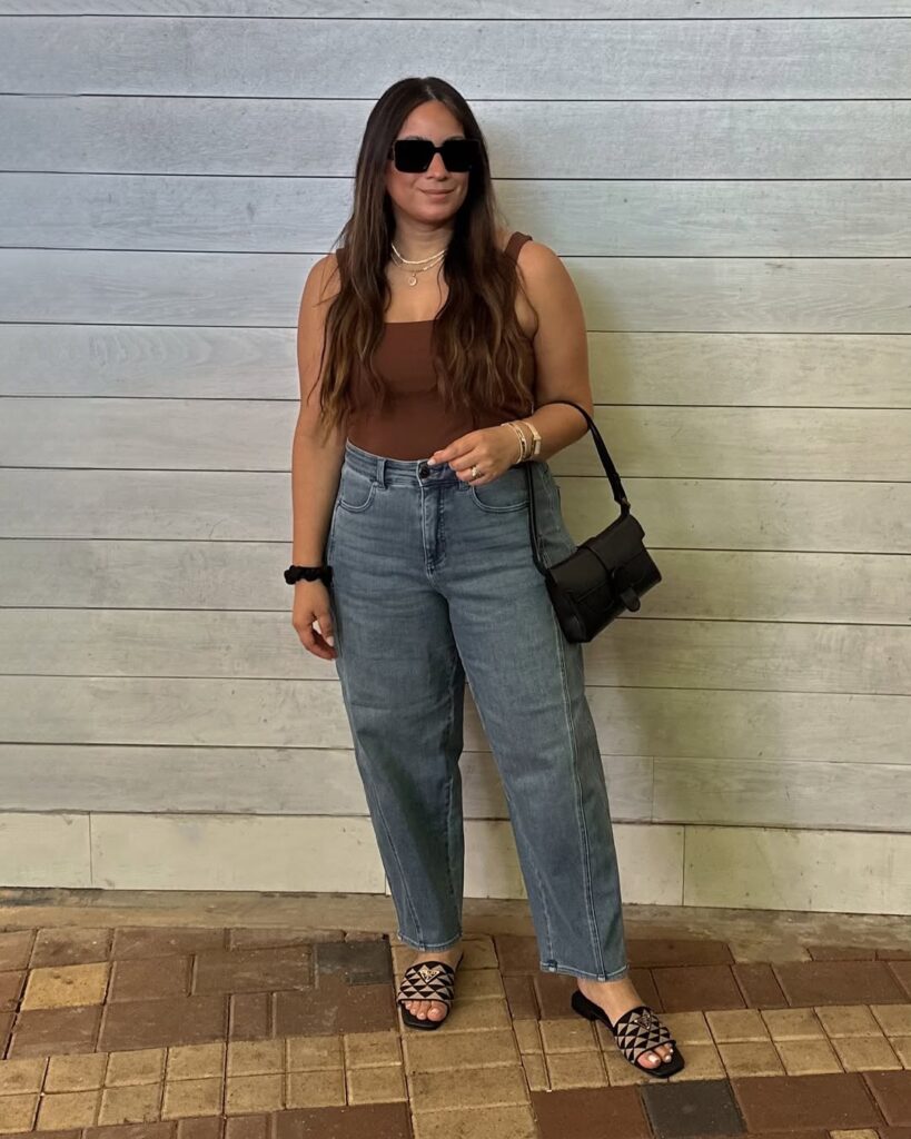 Minimalist look with a brown tank top, high-waisted straight-leg jeans, black mini shoulder bag, black sandals, and chunky sunglasses.