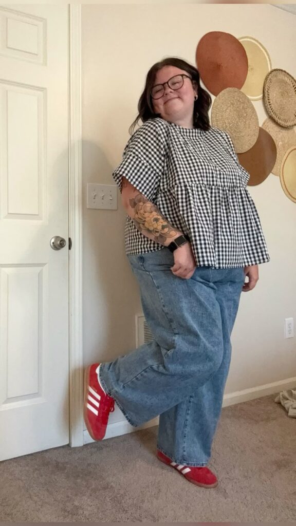 Gingham peplum blouse paired with relaxed blue jeans and bold red Adidas sneakers, styled with glasses and a floral arm tattoo.