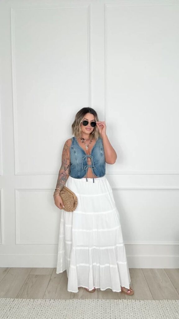Boho-inspired outfit featuring a denim lace-up crop top and a tiered white maxi skirt, accessorized with a straw clutch and sunglasses.

